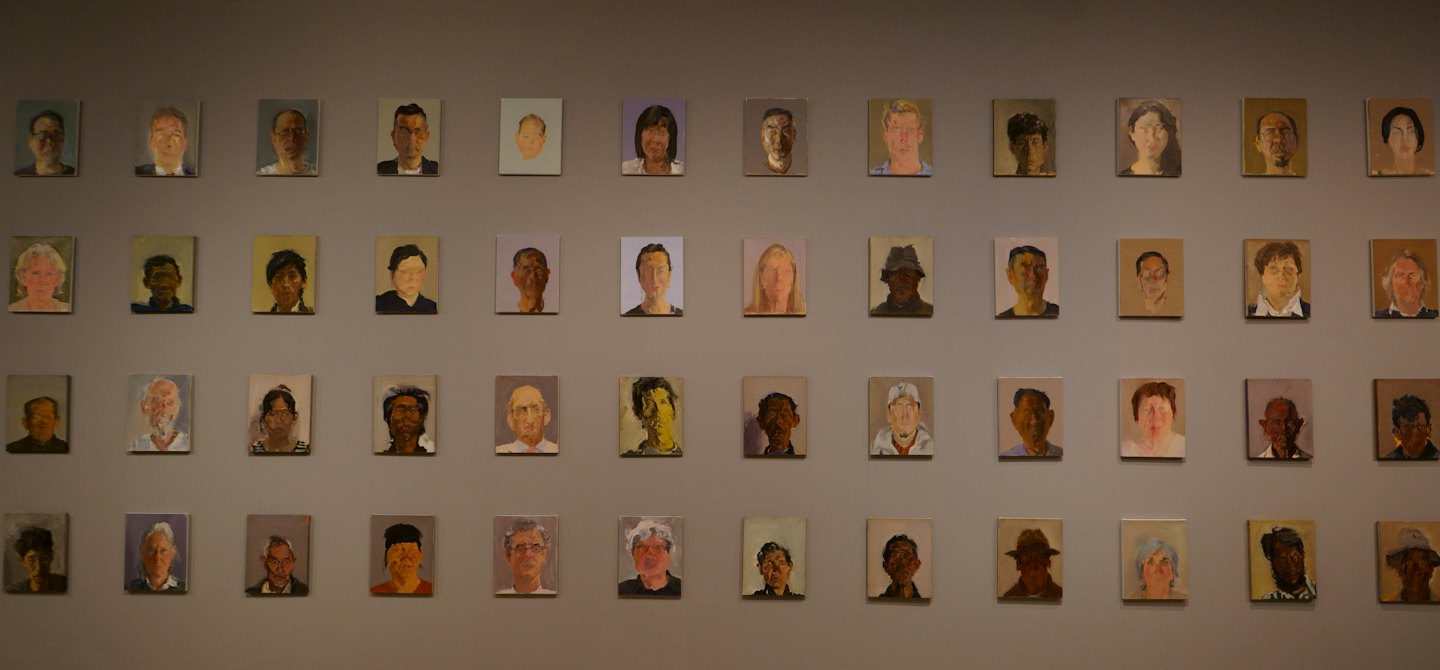 Fifty-five portrait paintings are arranged in a grid on a wall.