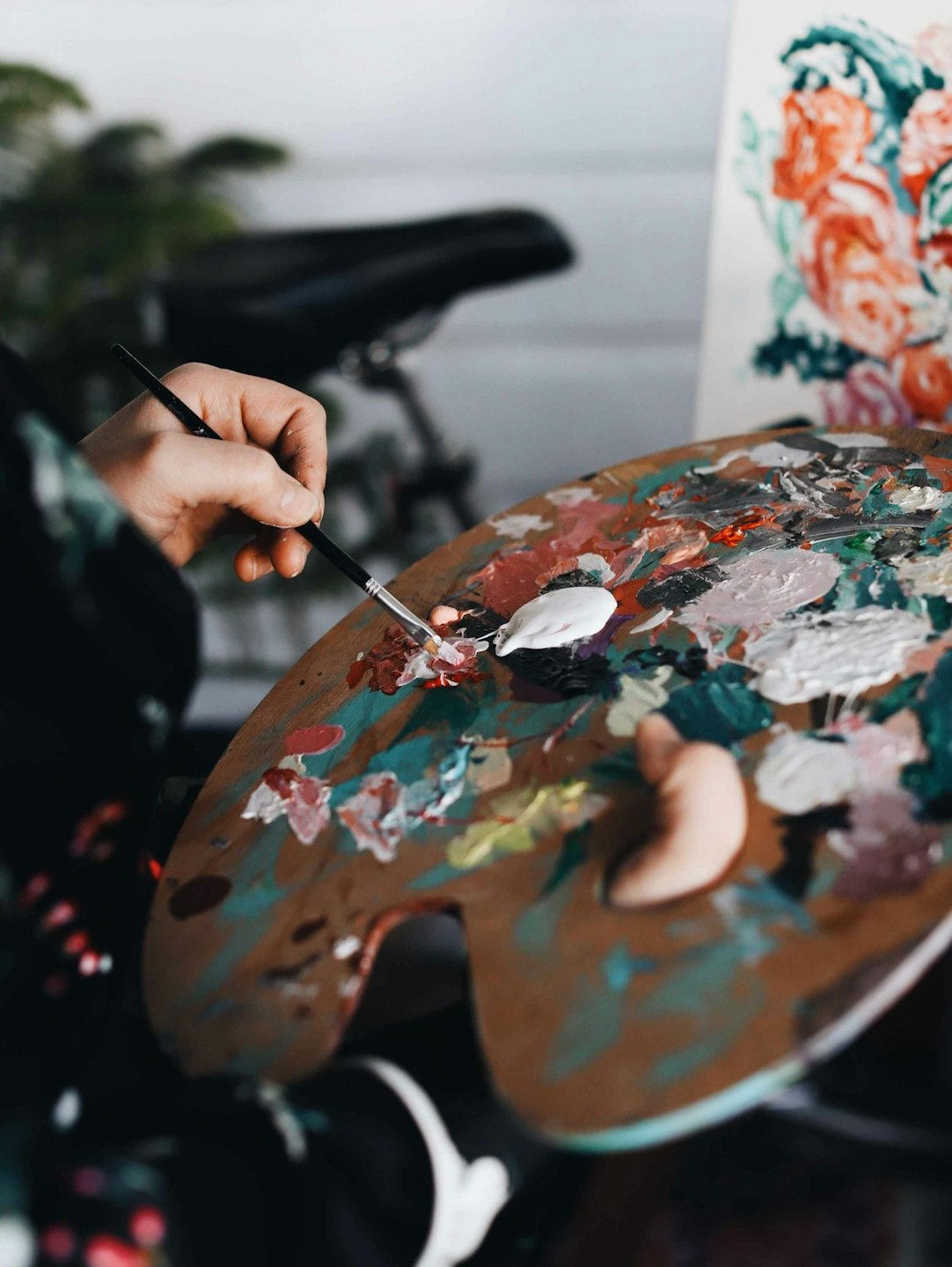 Artist's hand mixes paint on a wooden palette with a canvas in the background.