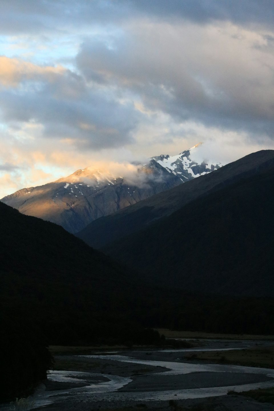 A winding river flows past forested banks towards snow-capped mountains.